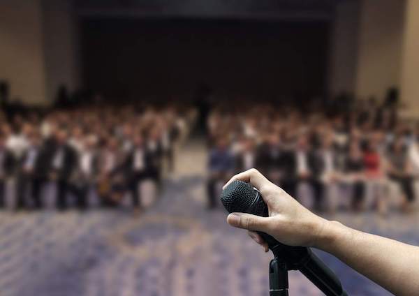 Eine Hand an einem Mikrofon vor Zuschauern.